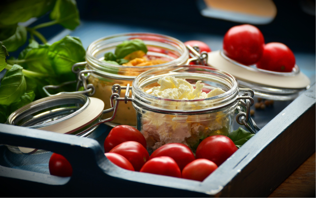 Three salads in a jar surrounded wih cherry tomato and spinach leafs